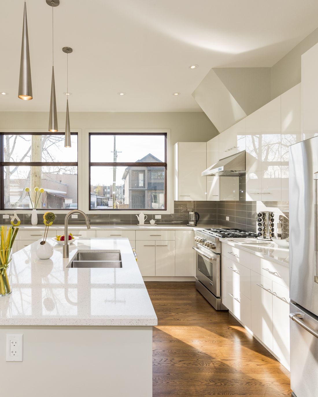 A bright kitchen with white cabinets, a stone island and pendant lights