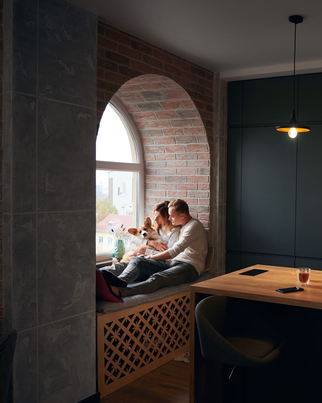 A couple and their dog relaxing in an arched window seat in a loft kitchen