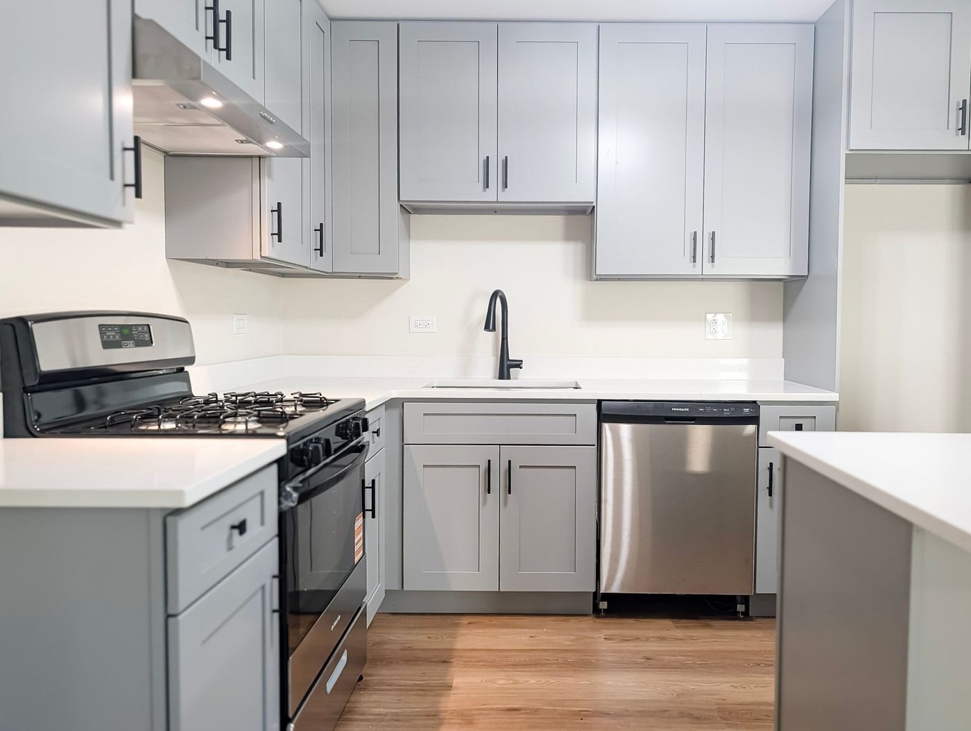 A newly renovated kitchen with gray shaker cabinets, white counters and stainless appliances
